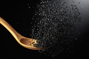 Grains of black sesame is poured with a wooden spoon.