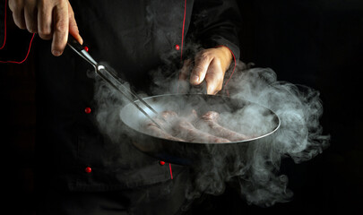 Meat sausage is fried in a frying pan in the chef hand. Free space for advertising on black...