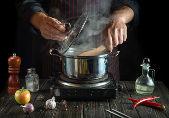 Professional chef cooks a delicious soup with vegetables in a hot pot. Work environment on the kitchen table. Menu for the hotel or restaurant