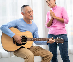 Senior man happy sitting playing acoustic guitar indoors as hobby after retirement. Elderly musician has fun singing a song with an instrument. Cheerful grandfather guitarist enjoys leisure activity.