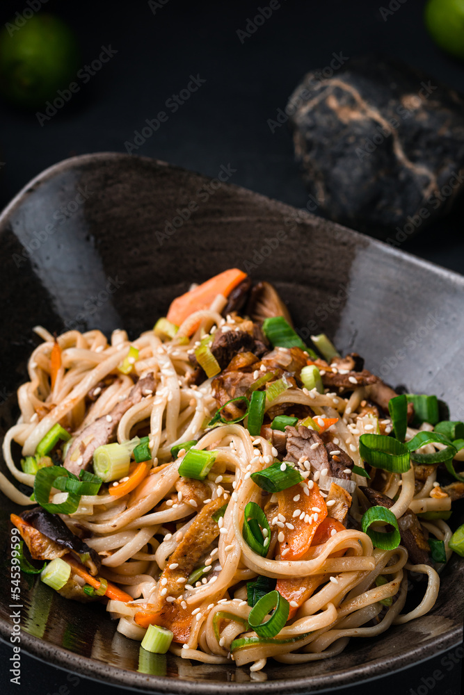 Sticker asian food udon noodles with teriyaki beef and vegetables: red pepper, tomatoes, onion and sesame se