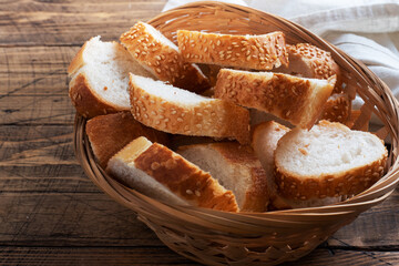 Fresh white bread, baguette slices in a wicker basket. Wooden rustic table background. Close up