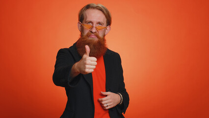 Like. Bearded redhead man in black jacket raises thumbs up agrees with something or gives positive reply recommends advertisement likes good. Young guy isolated alone on orange studio background