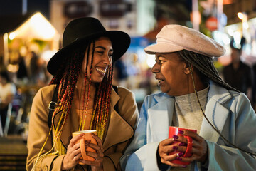 African mother and daughter having fun drinking hot chocolate outdoor in winter time - Focus on senior woman eye