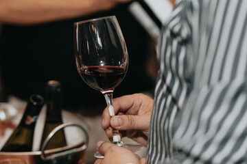 Glass of red wine held by a person at a premium wine tasting with friends and wine lovers.