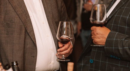 Glass of red wine held by a person at a premium wine tasting with friends and wine lovers.