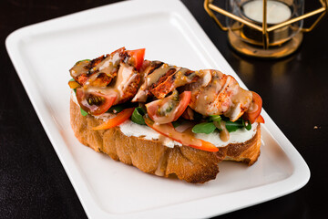 Italian snack bruschetta with fried chicken pieces, tomatoes, peppers, arugula, cream cheese and sauce.