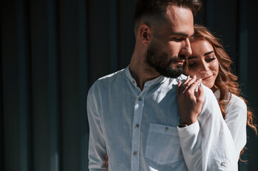 Embracing each other. Beautiful young couple is standing together against dark green background