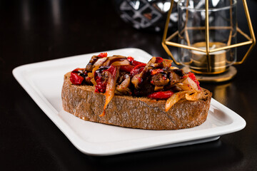 Bruschetta with eggplant, tomatoes, sweet peppers, onions and sauce in a plate.