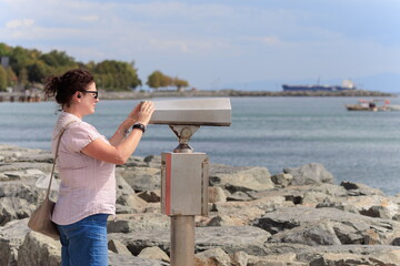Brunette woman looking through binoculars for a panorama of the sea and ships