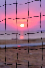 View of the sunset through the volleyball net. Dramatic sunset over sea.
