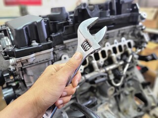 Naklejka premium Mechanic holding wrench for car engine repair with blur background