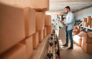 Machine operator is busy by setting up a device. Print house worker in white clothes is indoors