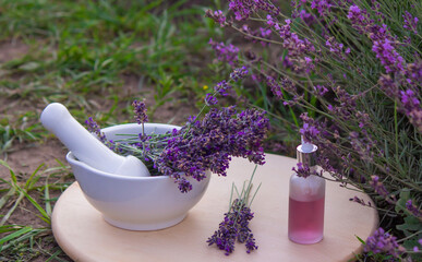 Fototapeta na wymiar A bottle of lavender essential oil on a wooden table and a field of flowers background.