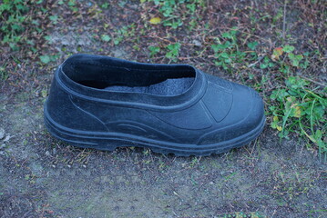 one old black dirty rubber galosh shoe stands on gray ground and green grass outdoors in nature