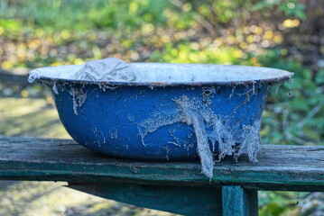 one old dirty blue metal enameled bowl in a white cobweb stands on a gray wooden table against a green background