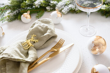 Beautiful Christmas festive table setting with white plate, champagne glass, golden balls and...
