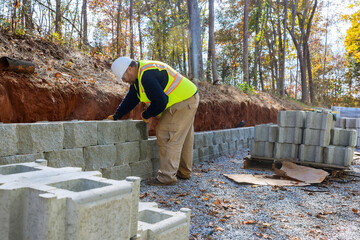 Man levels concrete block wall that is being built on new piece of property as part new retaining wall construction project