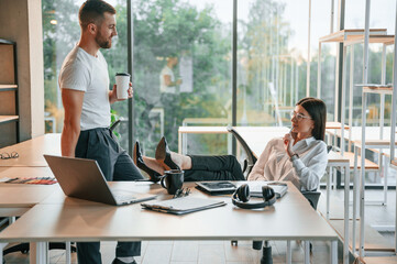 Relaxed, legs are on the table. Man and woman are working in the modern office together