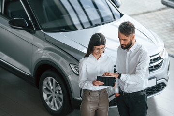 Fototapeta premium Having a business conversation. Man with woman in white clothes are in the car dealership together