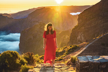 Beautiful woman in red dress walking barefoot on a very scenic hiking trail in the evening sun on...