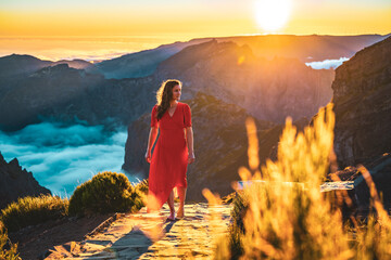 Beautiful woman in red dress walking barefoot on a very scenic hiking trail in the evening sun on...