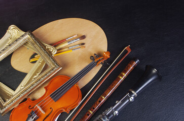 Art attributes. Music and painting. Violin, pipe, clarinet, art palette and brushes on a black...