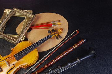 Art attributes. Music and painting. Violin, pipe, clarinet, art palette and brushes on a black background.