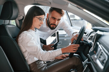 Woman sitting in the automobile. Man in white clothes are in the car dealership