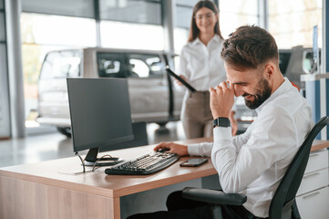 Obraz premium Man is sitting and smiling. Woman in white clothes in the car dealership