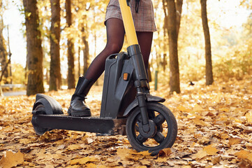 Obraz premium Close up view of woman's legs that are on the electric scooter in the forest at autumn season