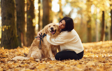 Embracing the animal. Woman is on the walk with her dog in the autumn forest at daytime