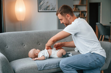 Father with toddler is at home, taking care of his son. Changing diapers - obrazy, fototapety, plakaty