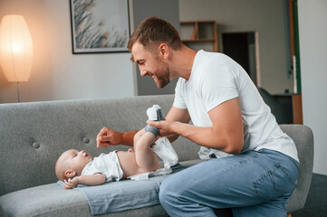 Father with toddler is at home, taking care of his son. Changing diapers - obrazy, fototapety, plakaty