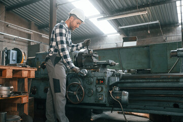 With manufacturing machine. Factory male worker in uniform is indoors