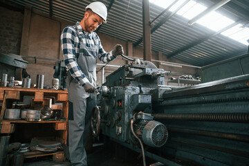 With manufacturing machine. Factory male worker in uniform is indoors