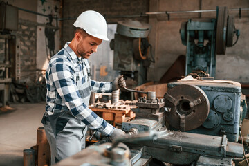 Fototapeta na wymiar Side view. Operating the machine. Factory male worker in uniform is indoors