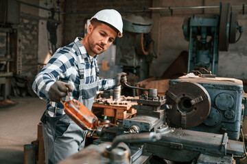 Handyman is working with factory machine. Warehouse employee in uniform is indoors