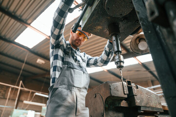 Factory male worker in uniform is indoors. Operating the drill machine