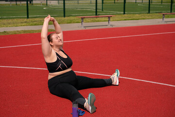 A young plump woman does stretching by raising her arms above herself while sitting on the rubber...