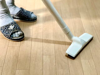 木目調の床に掃除機をかける足元