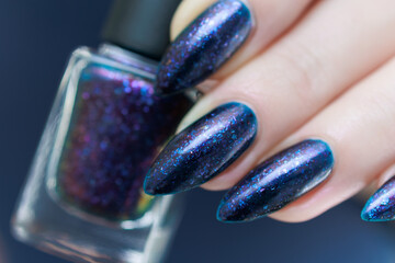 beautiful female hand with long nails and purple blue manicure with bottles of nail polish