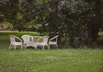 Empty and white garden table and chairs in a garden in greenery. Garden furniture set. Garden decoration	