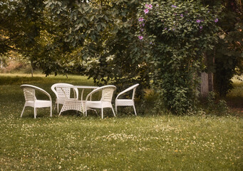 Empty and white garden table and chairs in a garden in greenery. Garden furniture set. Autumn concept. Garden decoration	