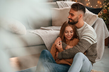 Man is embracing his woman from behind. Lovely young couple are celebrating New Year at home