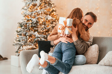 Woman is with gift box for the man. Lovely young couple are celebrating New Year at home