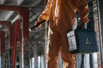 Holding case and flashlight. Man dressed in chemical protection suit in the ruins of the post...