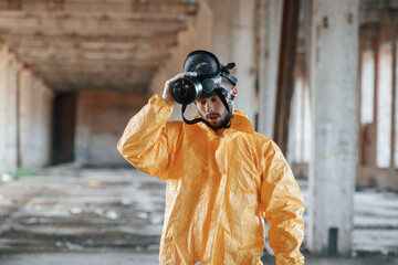 Taking off gas mask. Man dressed in chemical protection suit in the ruins of the post apocalyptic building