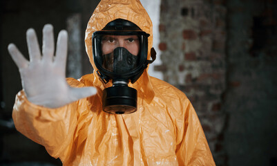 Stop sign by hand. Man dressed in chemical protection suit in the ruins of the post apocalyptic...