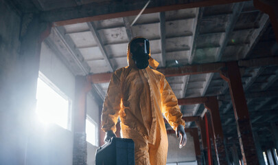 Walking with hard case. Man dressed in chemical protection suit in the ruins of the post...